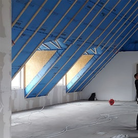 Zwei Handwerker arbeiten im Dachgeschoss eines Hauses. Einer der Männer steht auf einer Leiter.