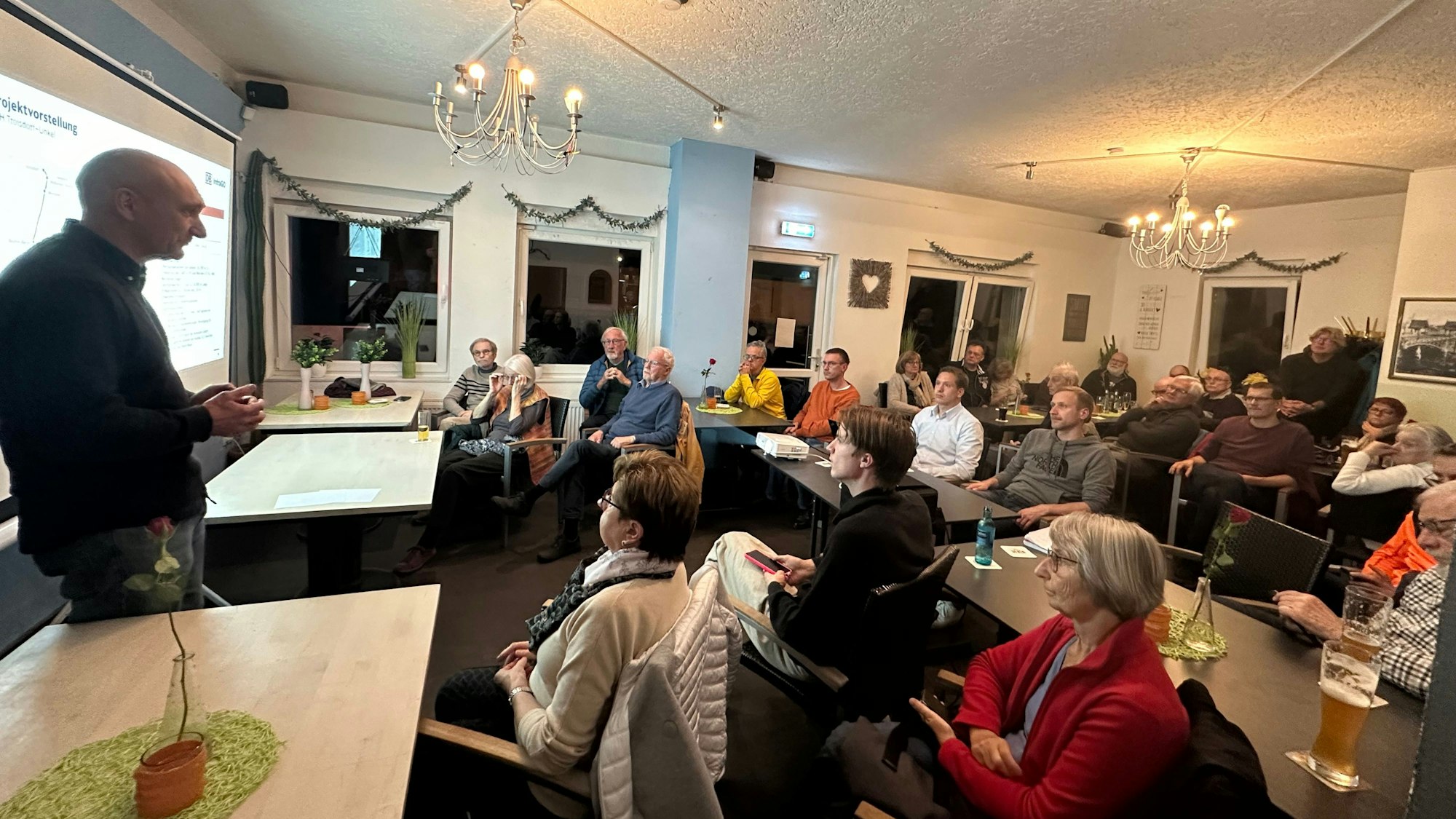 In der Gaststätte „Am Bahnhof“ sitzen Menschen dicht gedrängt und hören einem Vortrag von Jens Sülwold zu.