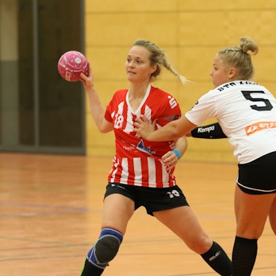 Eine Handballerin spielt einen Pass, eine Gegenspielerin fasst ihr an die Brust.
