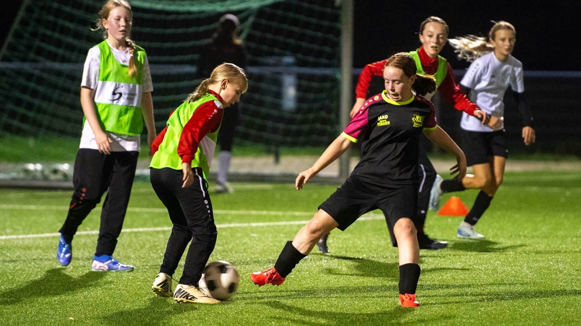 Junge Fußballerinnen trainieren im Flutlicht.