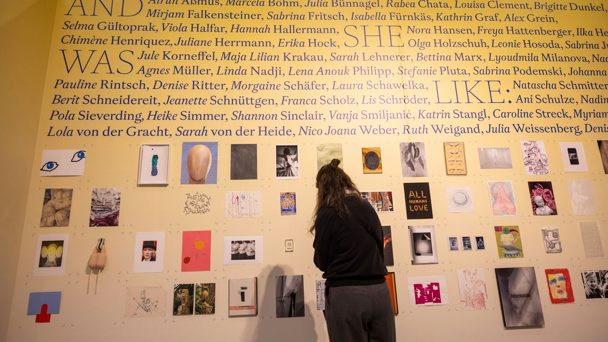Eine Besucherin steht vor der ·Wall of Bäm·, eine sechs Meter lange Wand, auf der Arbeiten von über 60 Künstler*innen verschiedener Generationen aus den Bereichen Bildende Kunst, Fotografie, Illustration und Design zeigen. Alle Werke kosten 400 EUR.