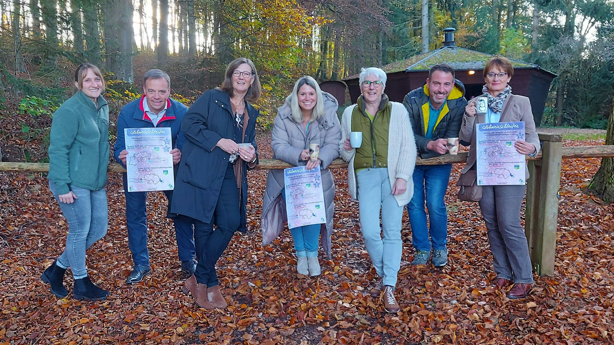Eine Gruppe von sieben Menschn steht vor einer Grillhütte im Herbstwald.