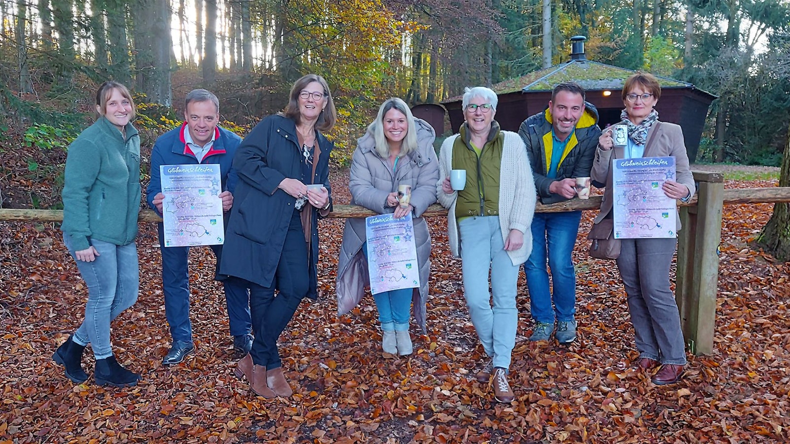 Eine Gruppe von sieben Menschn steht vor einer Grillhütte im Herbstwald.