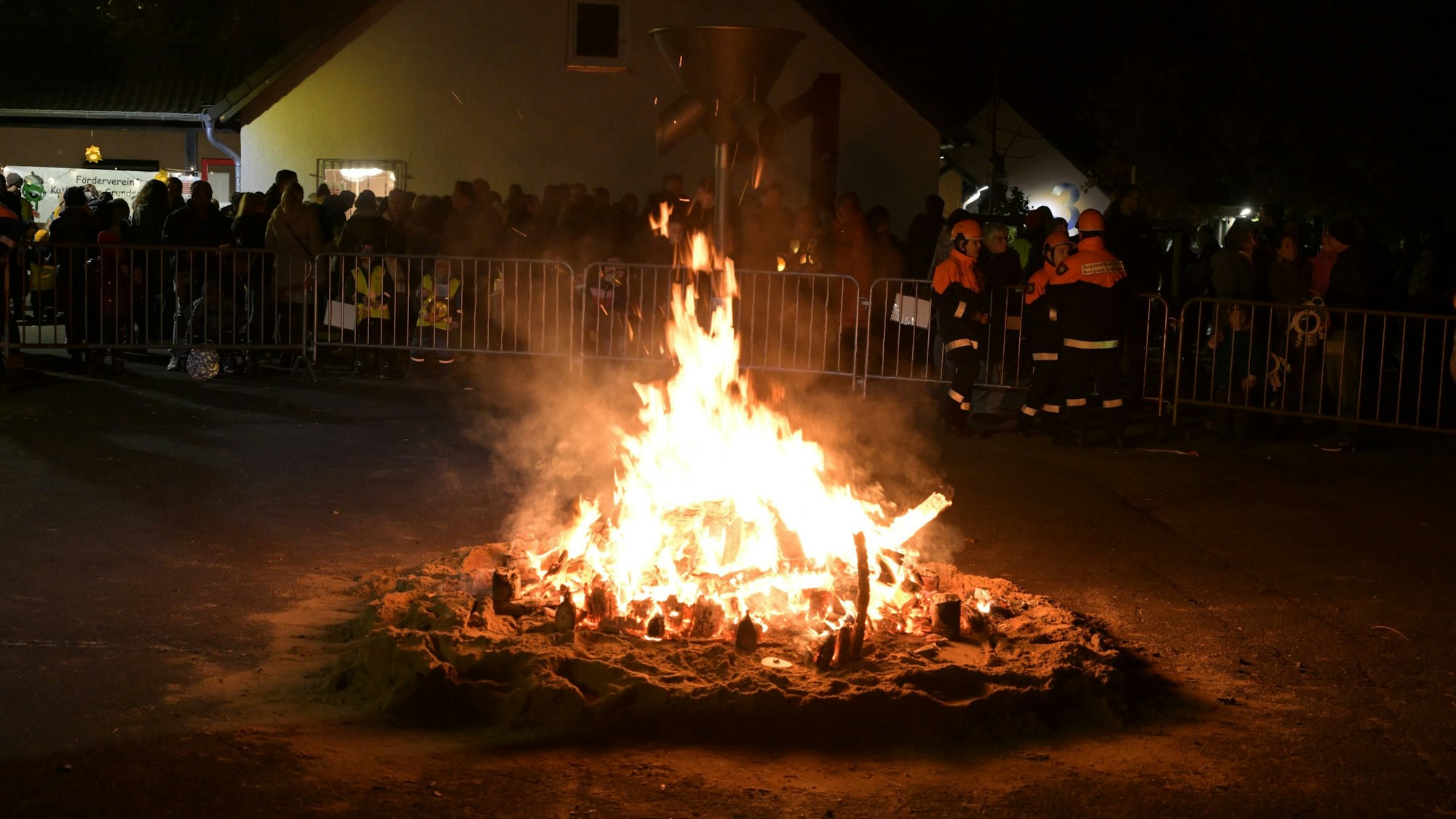 Im Vordergrund ist das Lagerfeuer. Hinter der Absperrung sieht man die Zuschauer.
