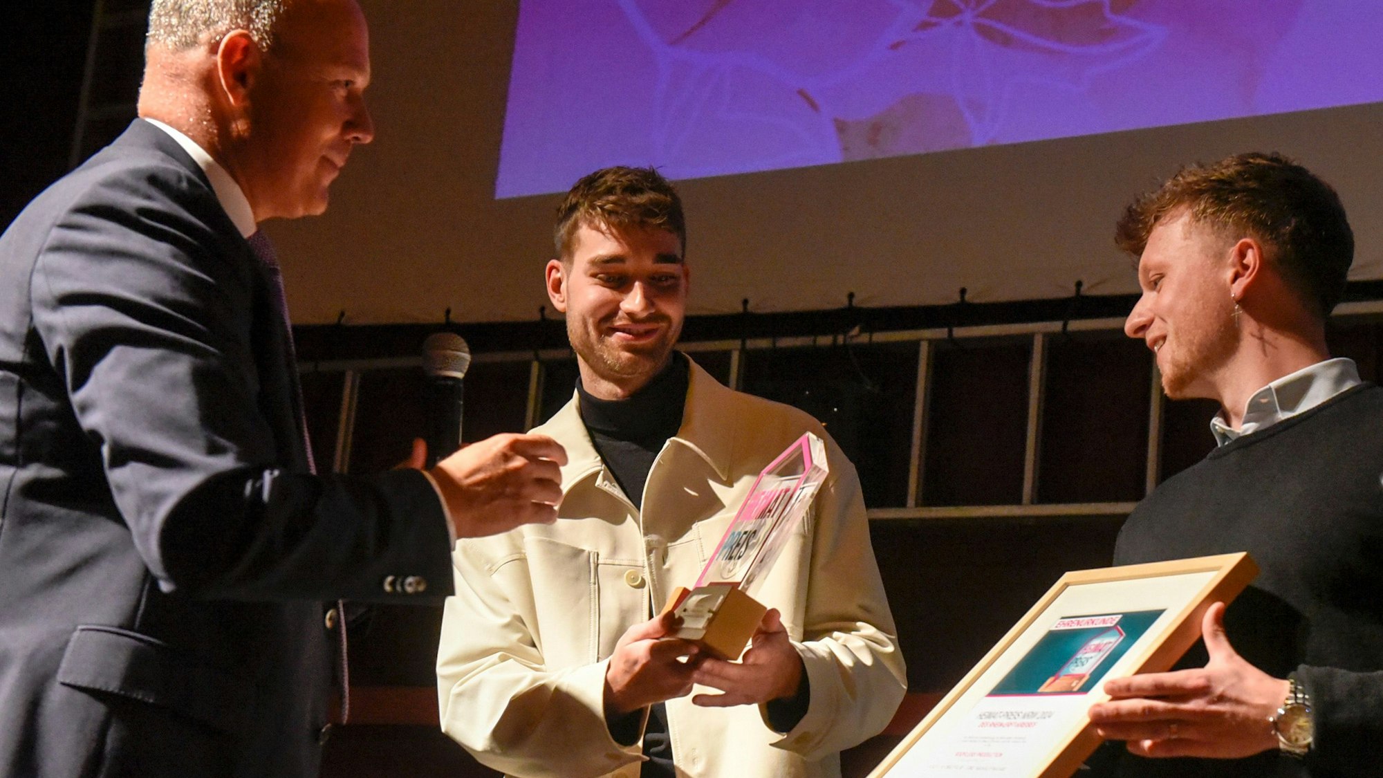 Das Foto zeigt zwei junge Männer, die einen Preis entgegen nehmen.