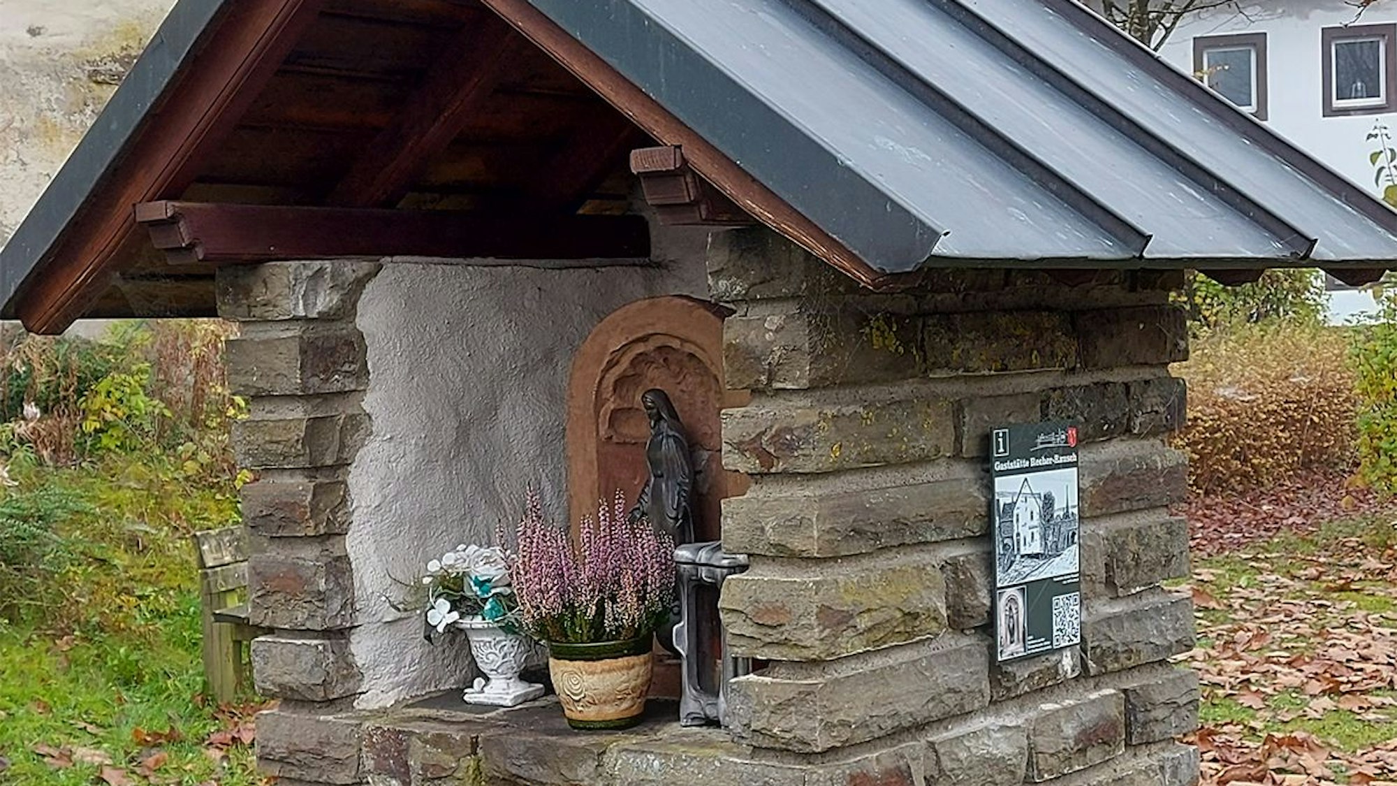 Eine Muttergottes steht in einem kleinen Häusschen aus Stein.