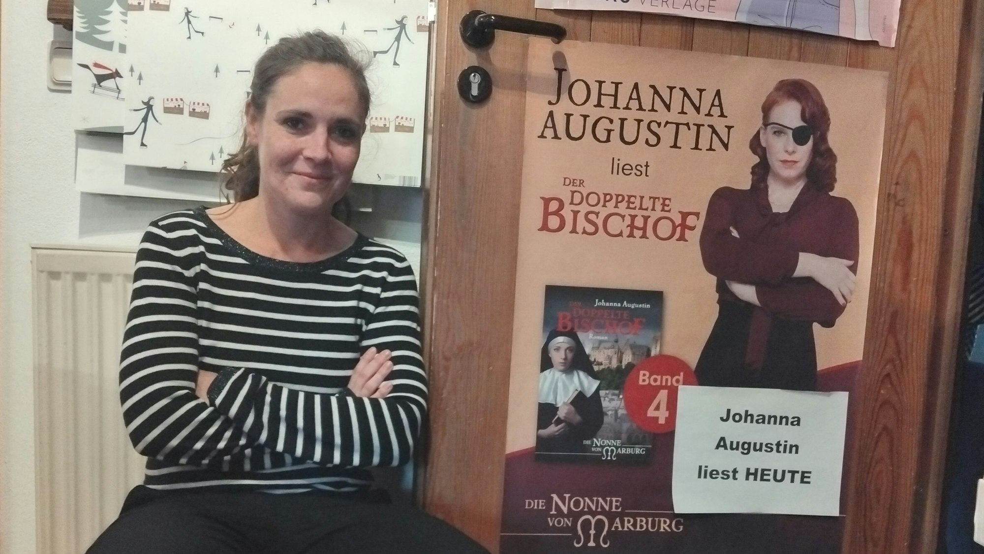 Eine Frau hockt mit verschränkten Armen neben einem Plakat, auf dem eine Frau mit ebenfalls verschränkten Armen zu sehen ist, die eine Augenklappe trägt. Ein Buch mit dem Titel „der doppelte Bischof“ ist neben ihr abgebildet.