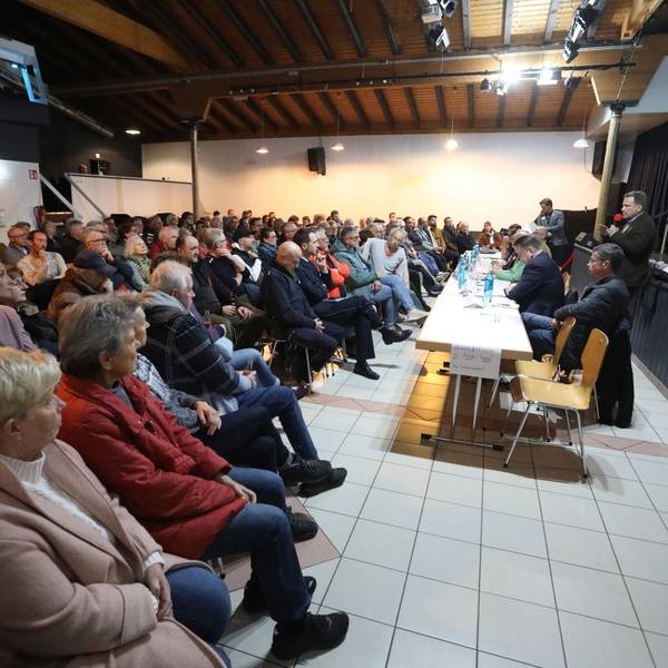 Zahlreiche Menschen sitzen in einem Saal und hören einem Mann mit Mikrofon zu.