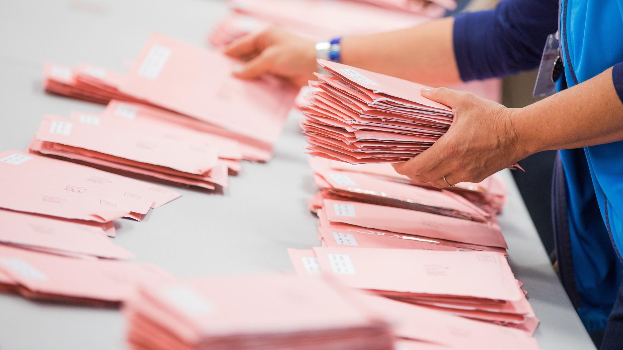 Das Bild zeigt Personen beim Sortieren von Wahlbriefunterlagen.