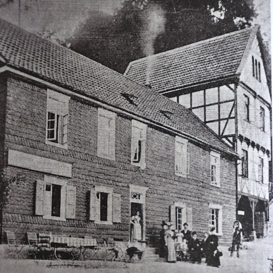 Ein bergisches Lokal, Ende des 19. Jahrhunderts. Davor ein gedeckter Tisch und eine Gruppe von Menschen im Sonntagsstaat