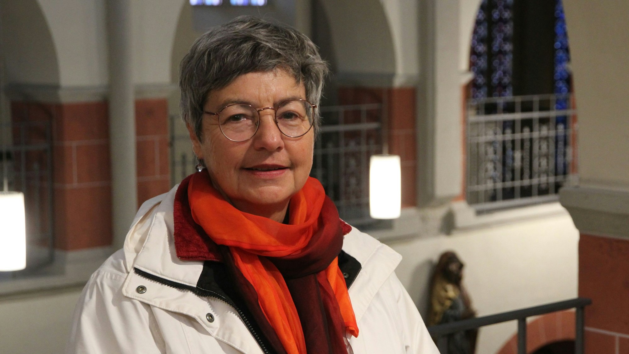 Eine Frau mit rotem Schal und heller Jacke auf der Empore einer Kirche