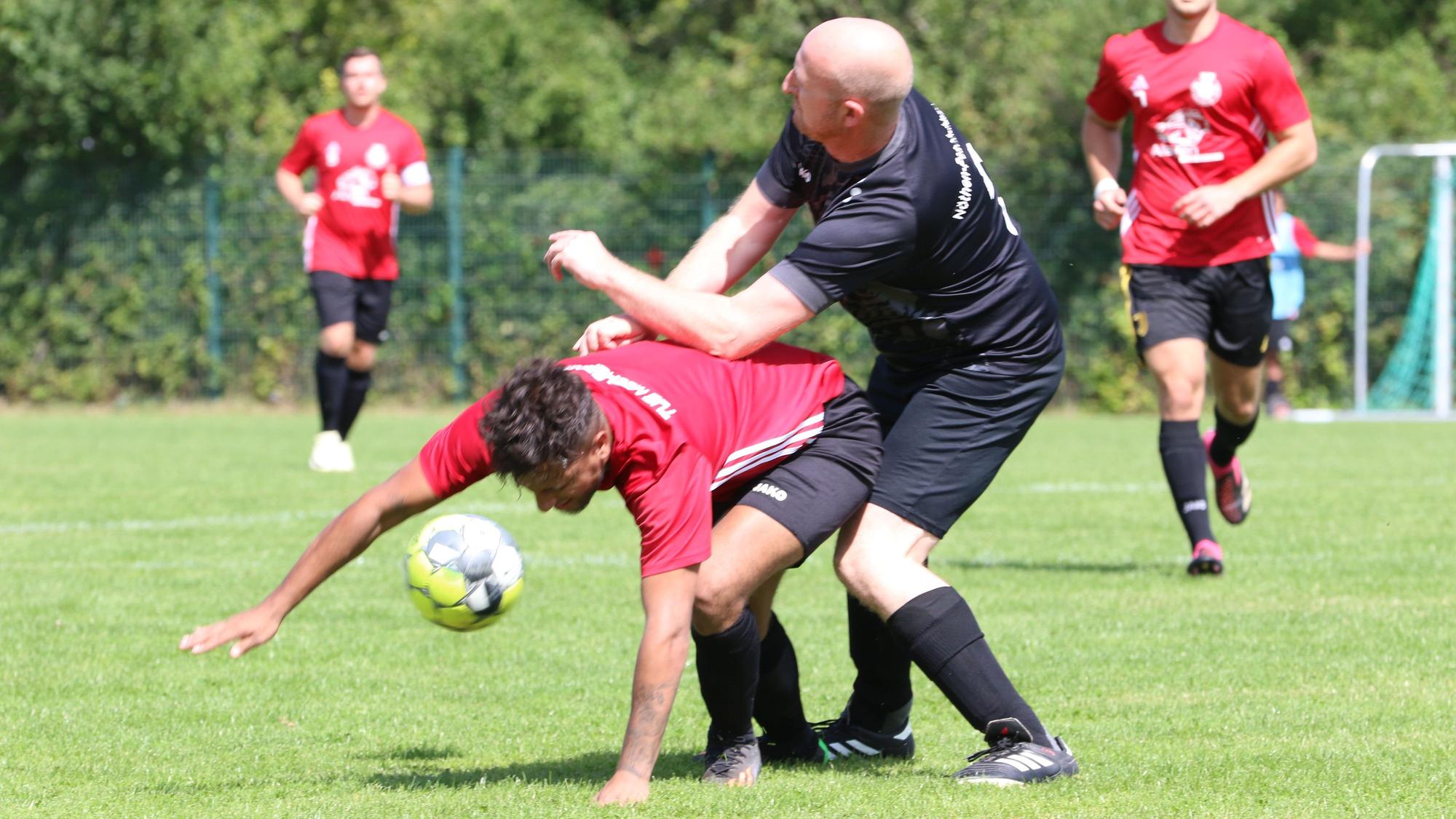 Schleidens Bürgermeister Ingo Pfennings als Fußballer im Zweikampf mit dem Mechernicher Adrian Meyer. Meyer stützt sich mit einer Hand auf dem Rasen ab.
