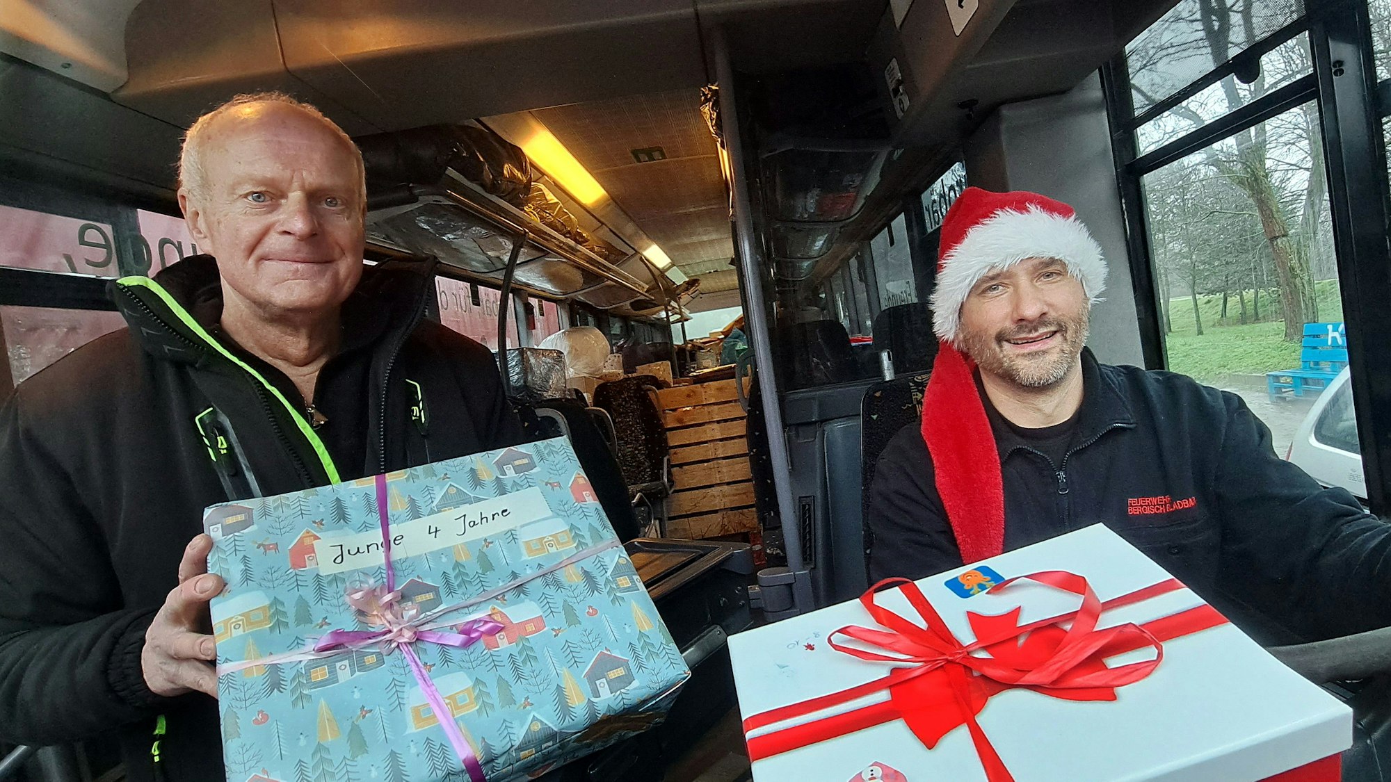 Zwei Männer sitzen mit Wichtelmütze und Paketen in einem Bus.