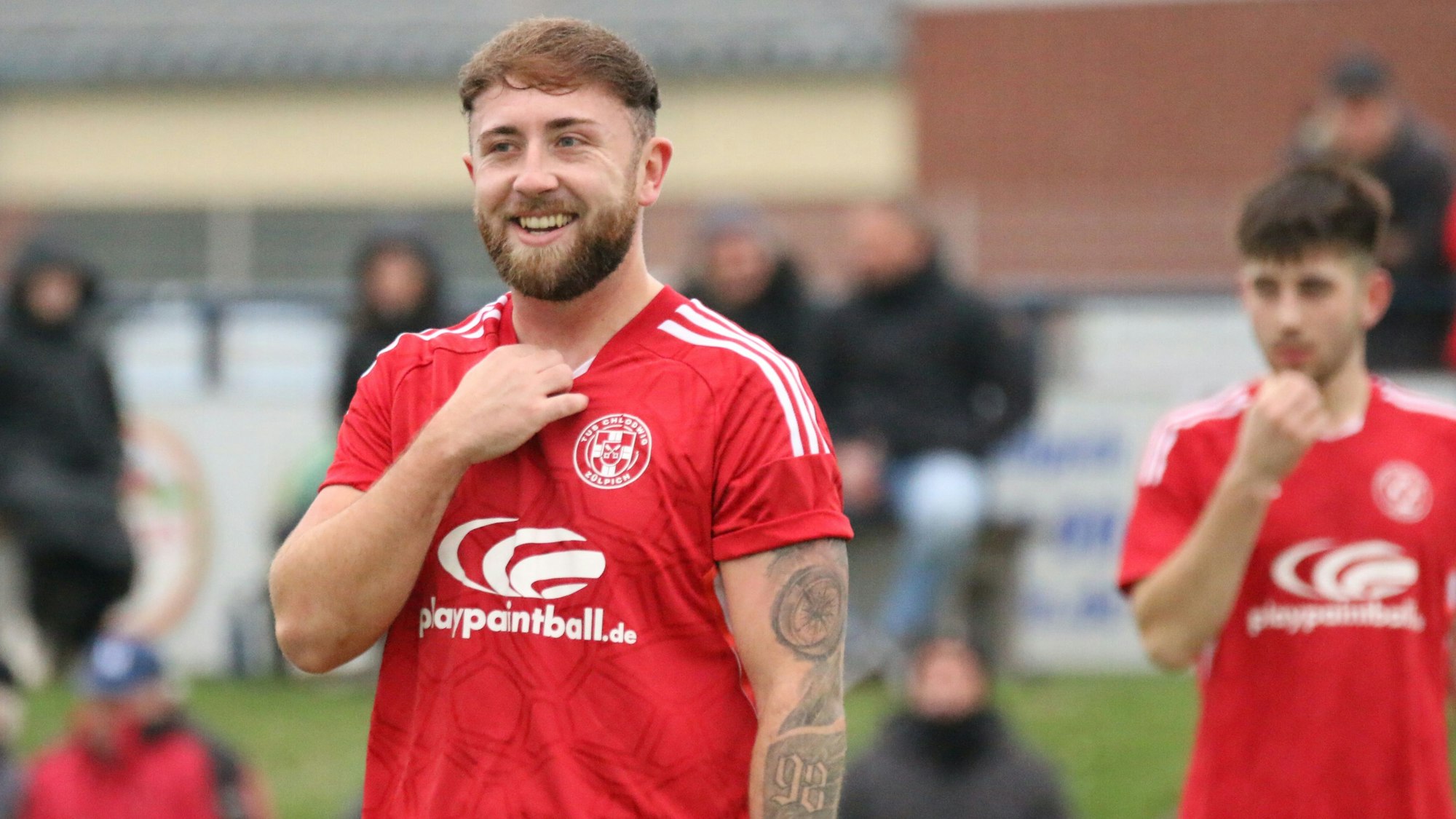 Ein Fußballer lächelt und greift sich mit der Hand an den Kragen des Trikots.