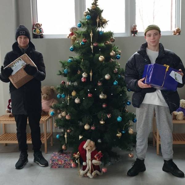Zwei Jugendliche halten Wichtelpäckchen in ihren Armen. Sie stehen neben einem Weihnachtsbaum.