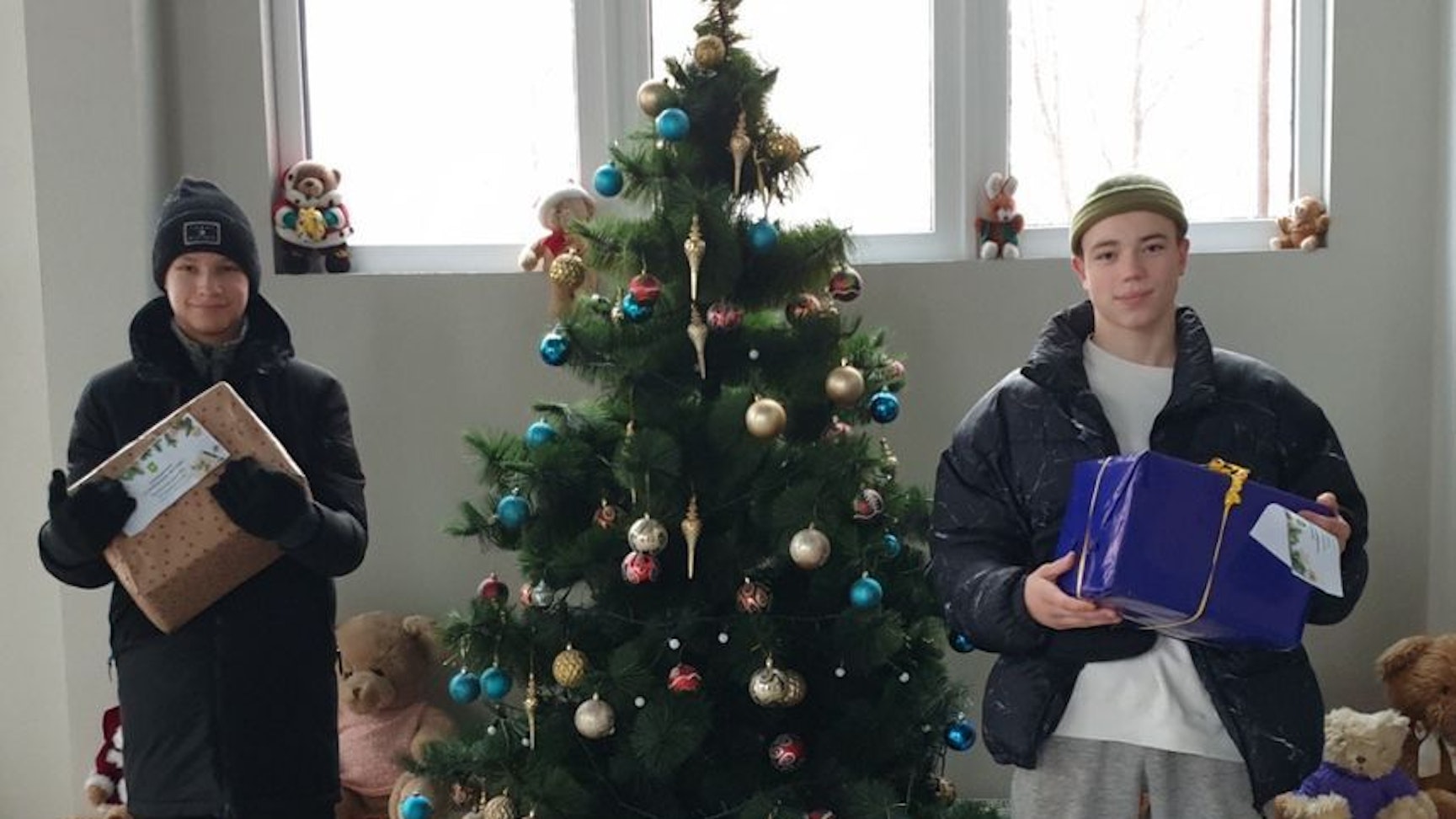 Zwei Jugendliche halten Wichtelpäckchen in ihren Armen. Sie stehen neben einem Weihnachtsbaum.