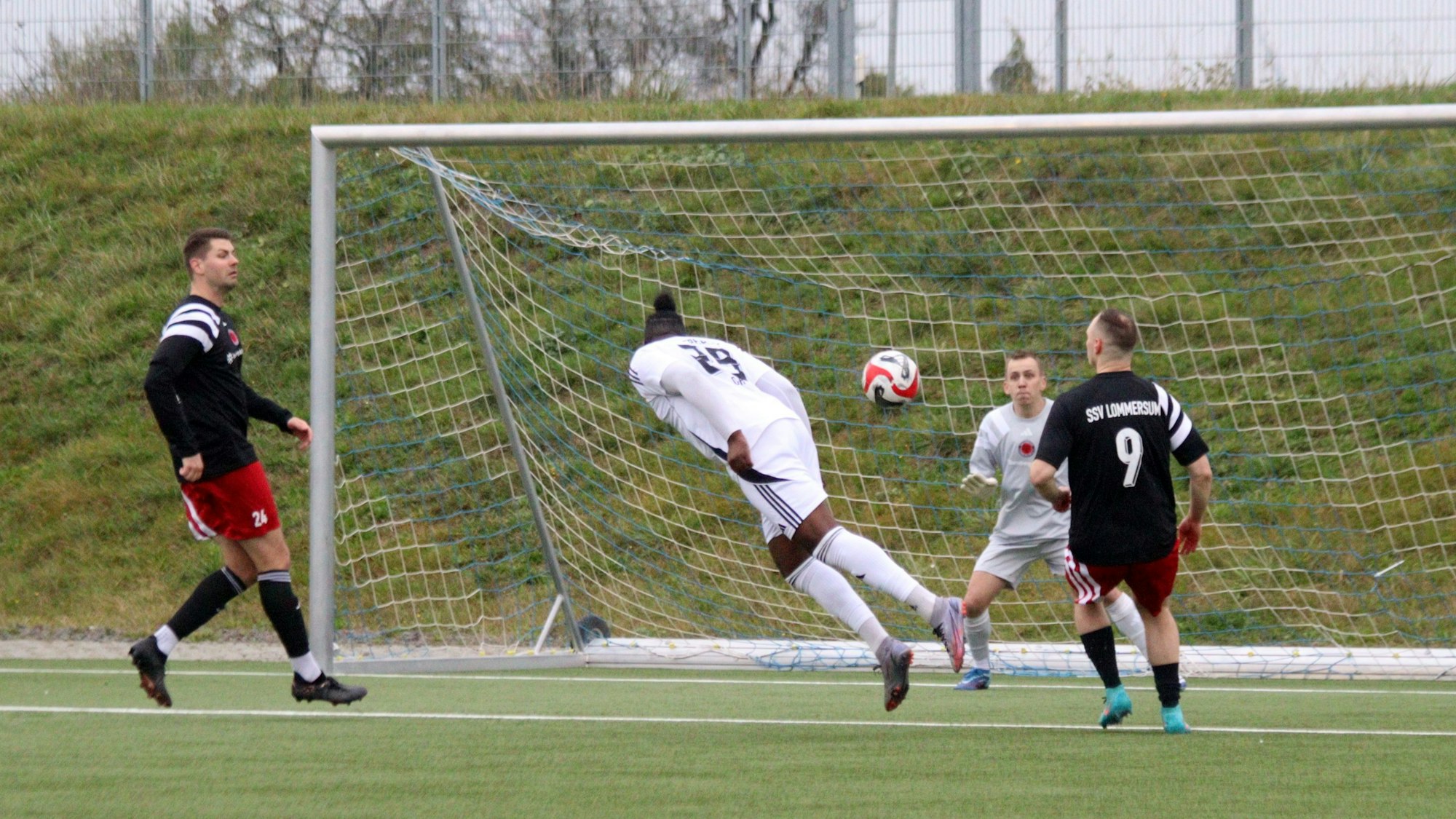 Ein Fußballer wirft sich in einen Kopfball. Zwei Gegenspieler schauen wie der Torwart nur zu.