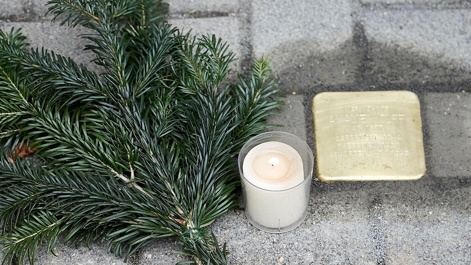 Ein neu verlegter Stolperstein, neben dem eine Kerze und ein Tannenzweig liegt.