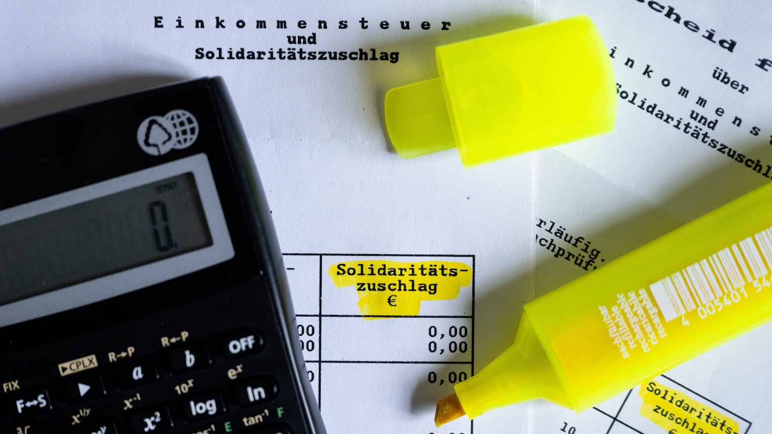 Das Wort ·Solidaritätszuschlag· ist neben einem Taschenrechner und einem Textmarker auf einem Steuerbescheid zu sehen.