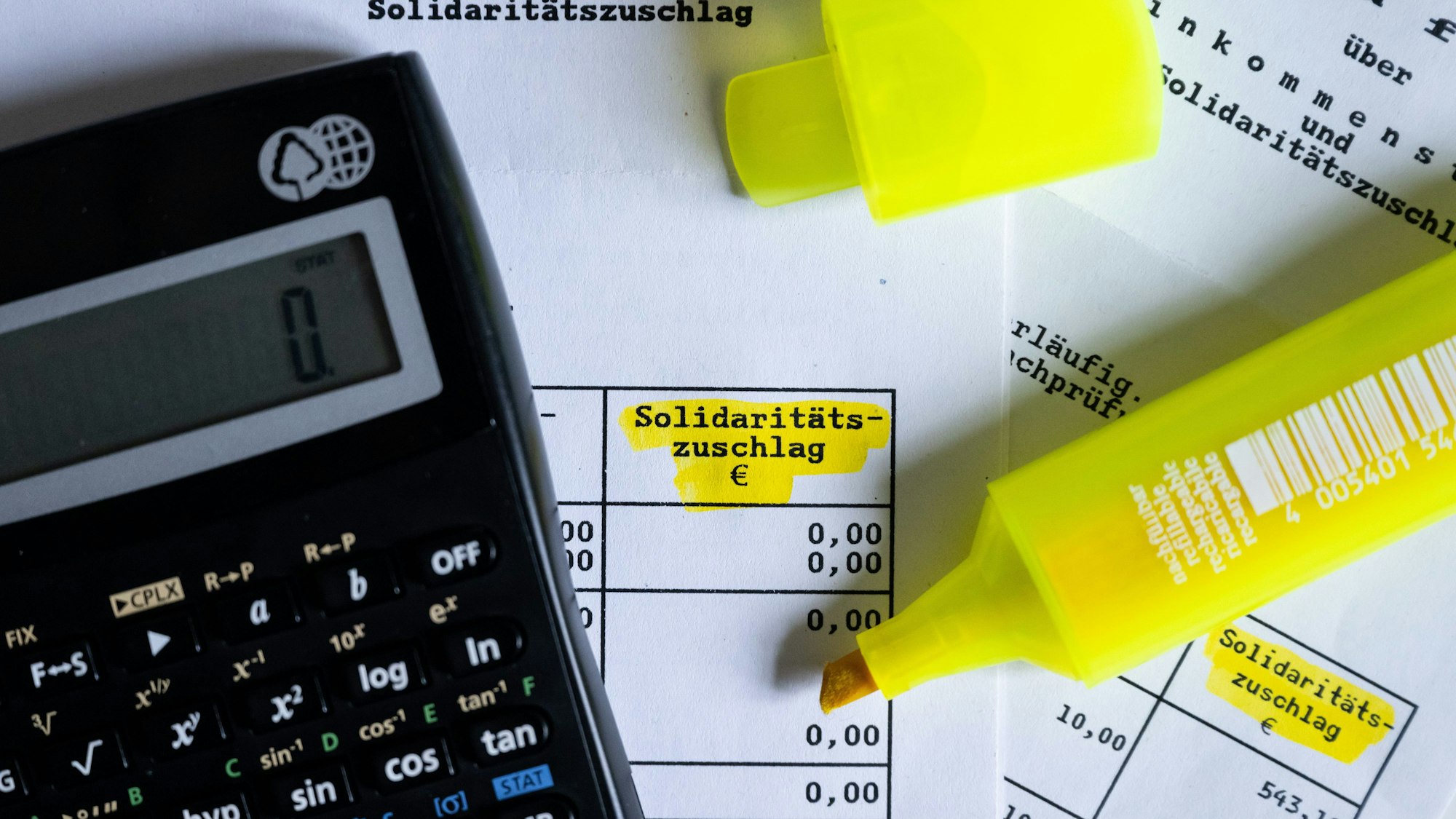 Das Wort ·Solidaritätszuschlag· ist neben einem Taschenrechner und einem Textmarker auf einem Steuerbescheid zu sehen.