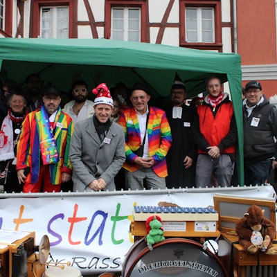 Kostümierte Menschen stehen auf einer Bühne unter einem Zelt.