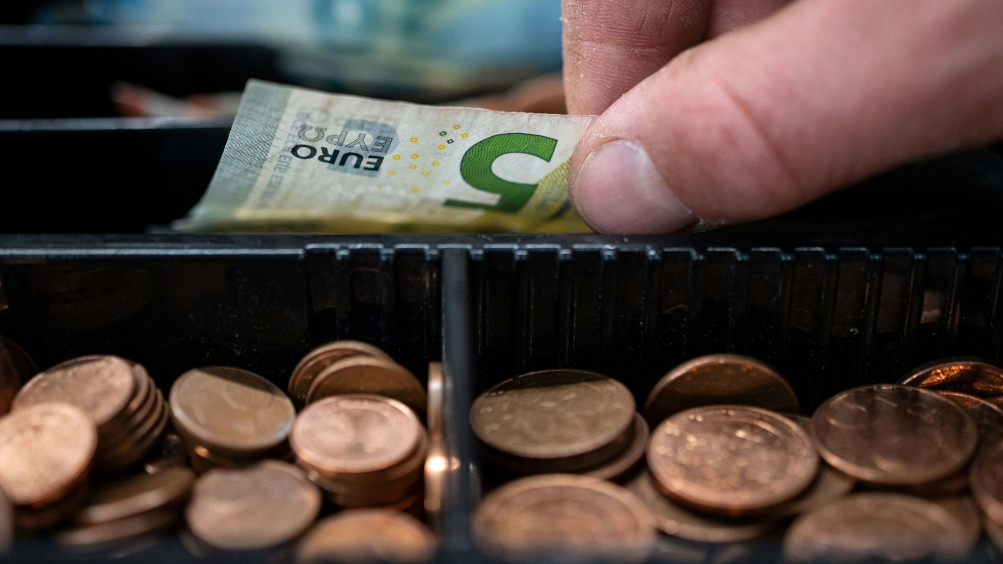 ARCHIV - 30.03.2022, Baden-Württemberg, Stuttgart: Ein Mitarbeiter eines Einzelhandelsgeschäfts nimmt einen 5-Euro-Schein aus einer Einkaufskasse.