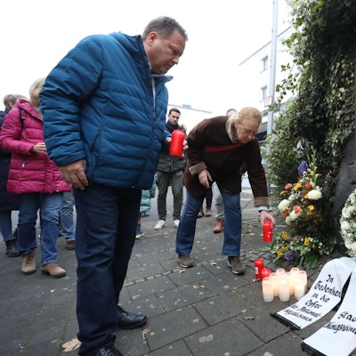 Kränze, Blumen und Kerzen vor einer Bronzetafel.