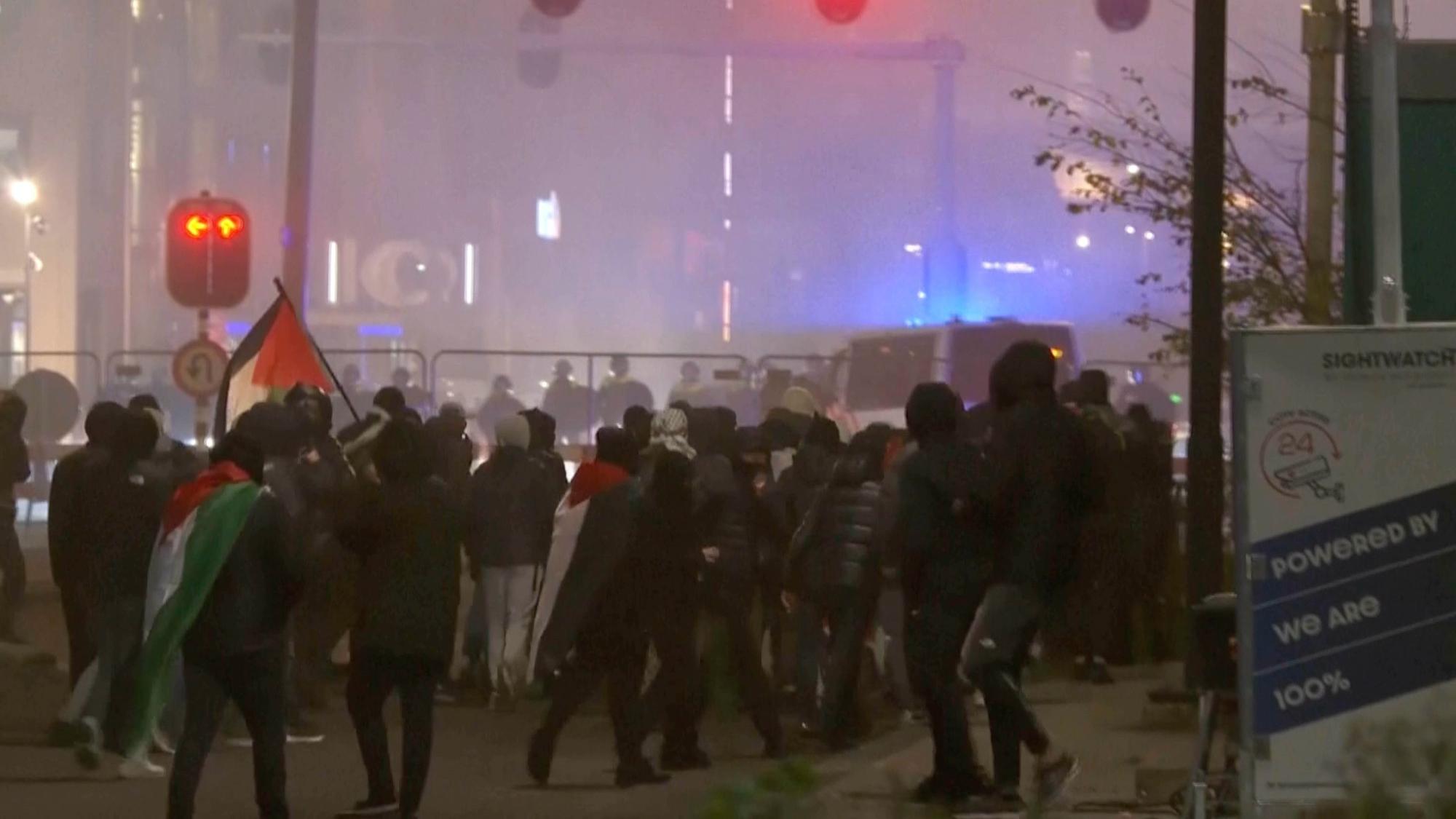 Amsterdam: Auf diesem Videostandbild geht eine Gruppe pro-palästinensischer Demonstranten in der Nähe des Fußballstadions in Amsterdam auf eine Polizeikette zu, während im Hintergrund Polizeiwagen fahren.