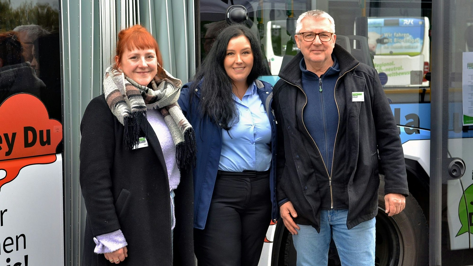 Zwei Frauen und ein Mann stehen freundlich lächelnd vor einem Linienbus.