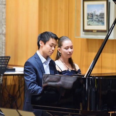 Eine junge Frau und ein junger Mann sitzen zusammen am Flügel.