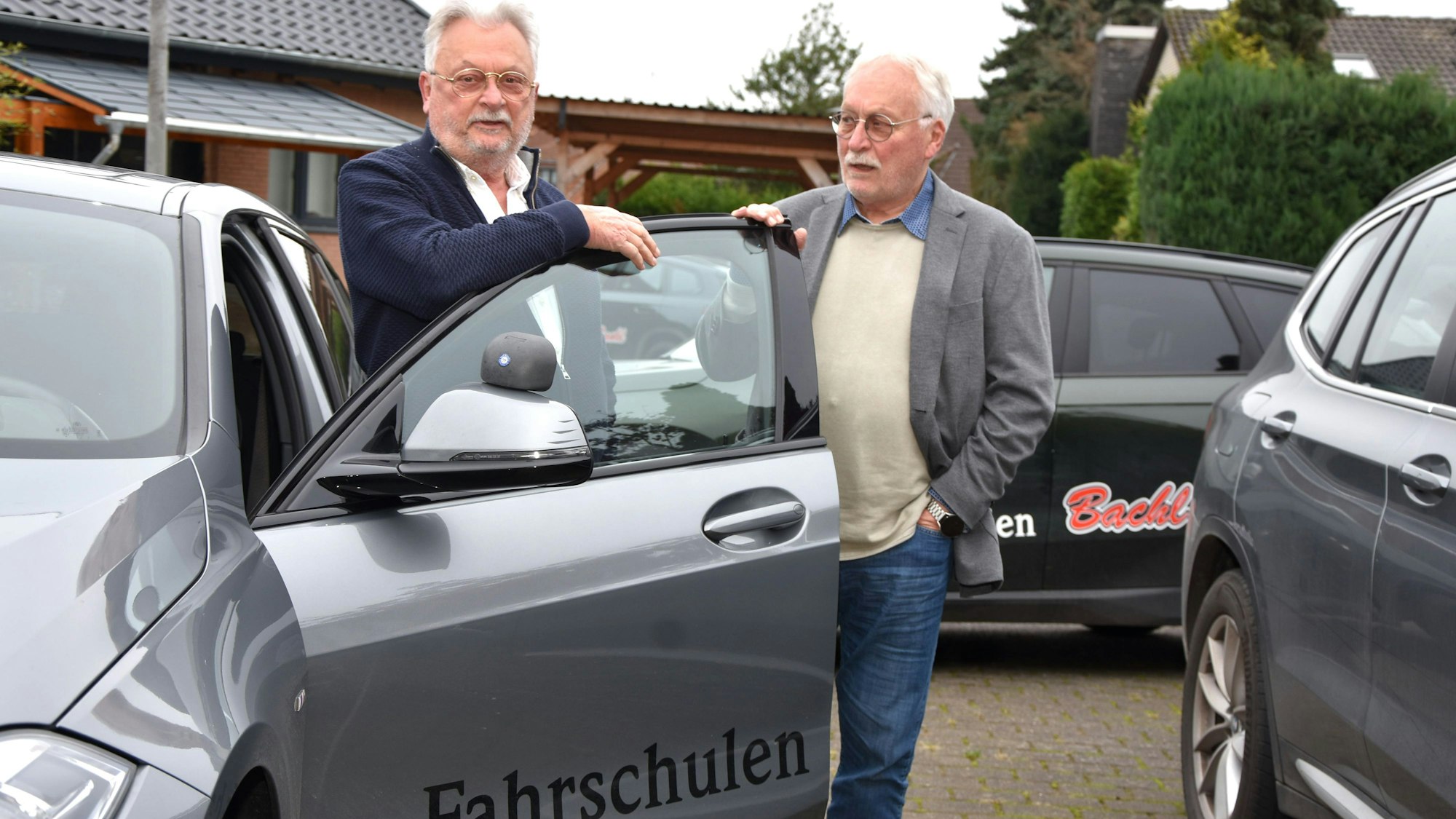 Zu sehen sind zwei Männer an einem Fahrschulauto.