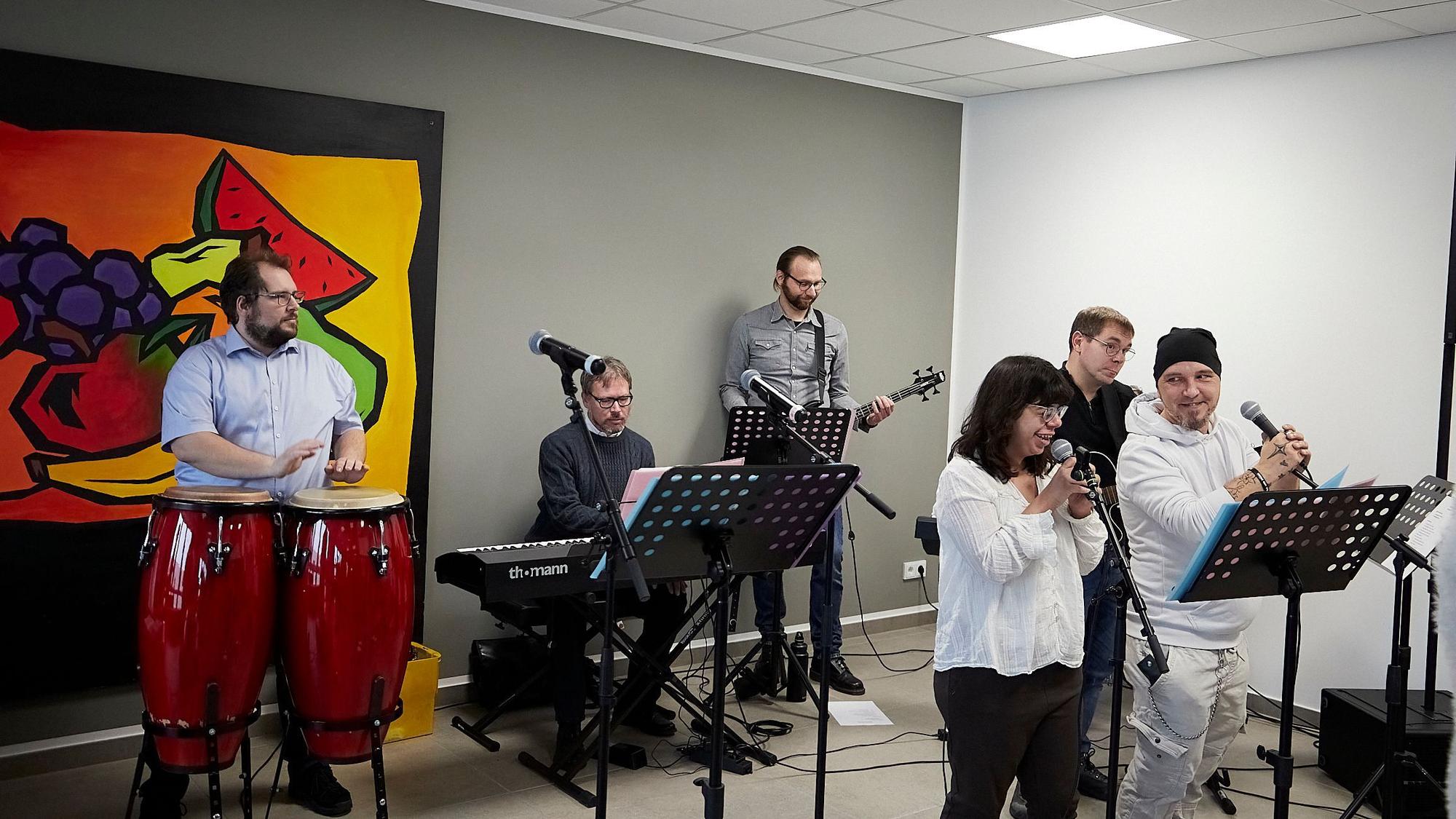 Vor einem Gemälde mit gemaltem Obst tritt eine Band auf.