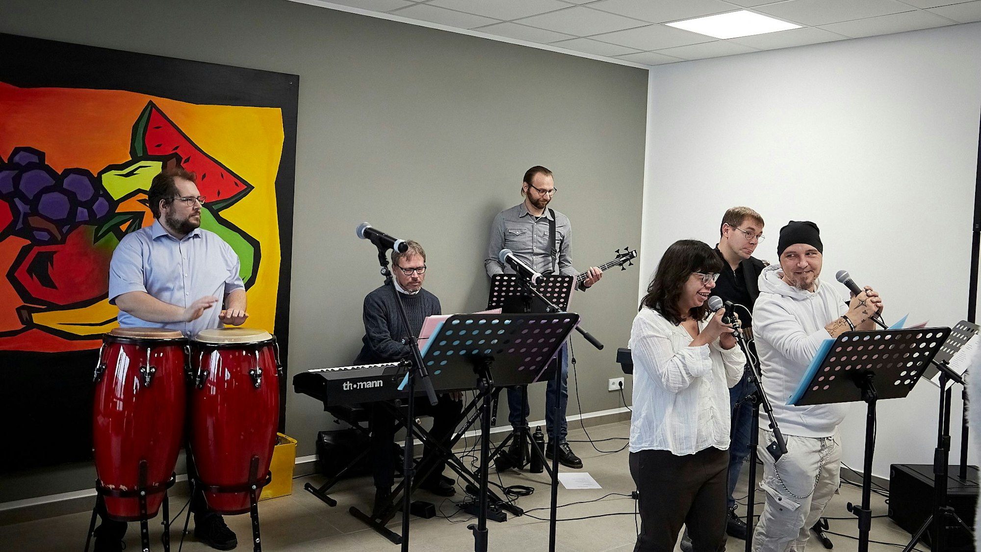 Vor einem Gemälde mit gemaltem Obst tritt eine Band auf.