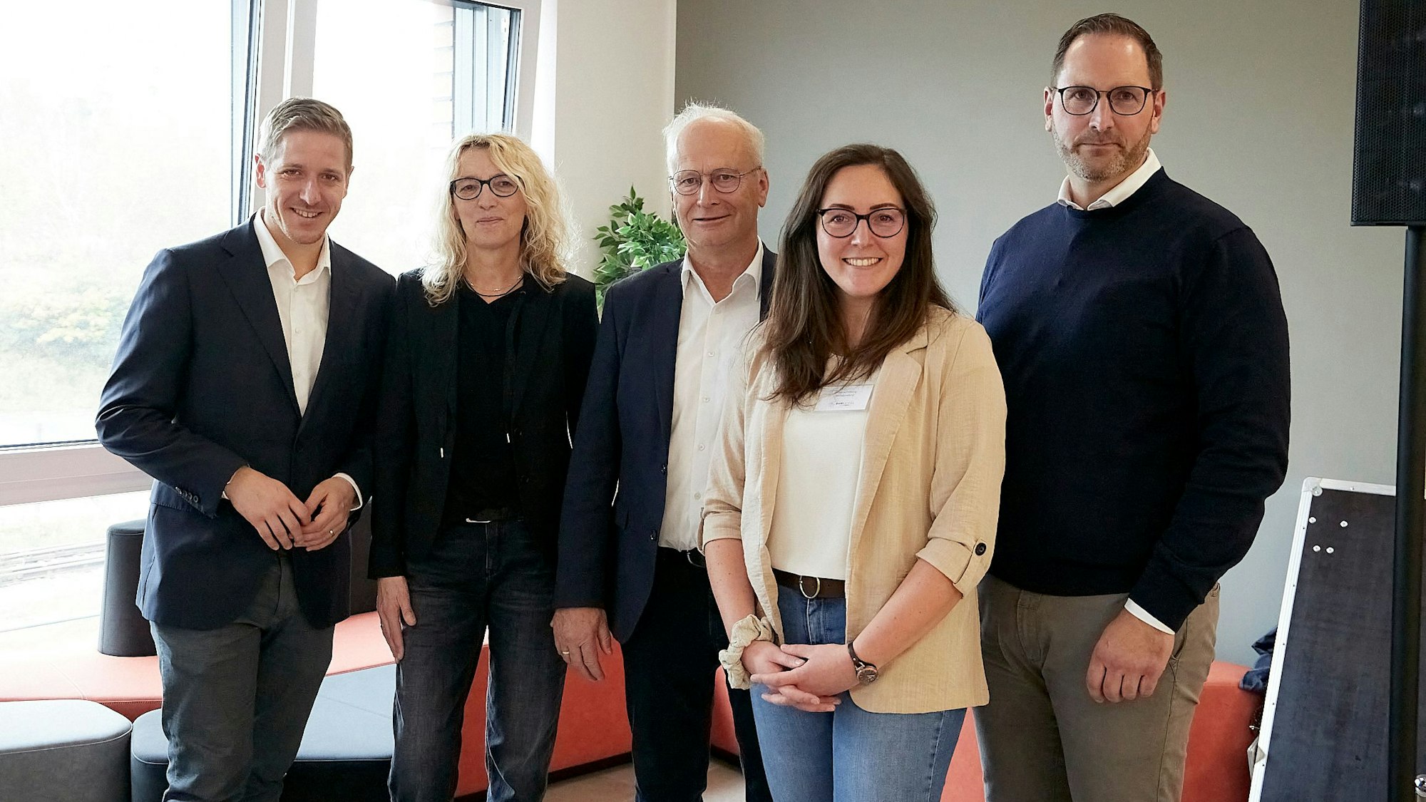 Fünf Personen stehen in einem lichtdurchfluteten Raum und schauen in Richtung der Kamera.