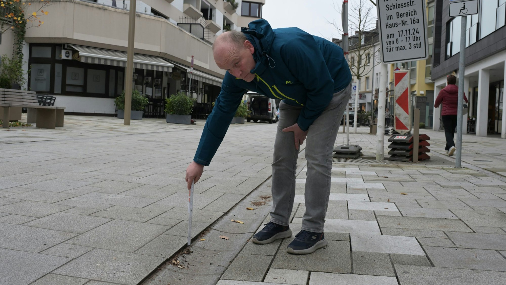 Der Schwiegersohn misst mit einem Zollstock den Höhenunterschied zwischen Bodenbelag und Pflasterstein.