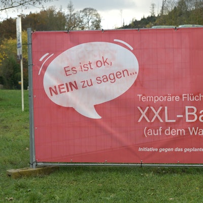 Ein rotes Protestplakat gegen den Bau einer Flüchtlingsunterkunft.