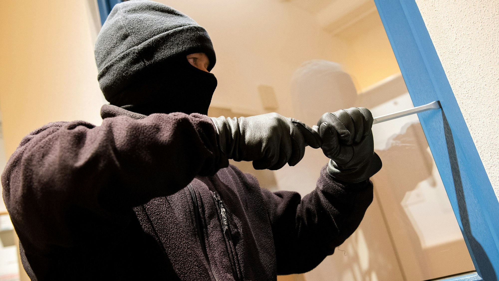 ARCHIV - 28.06.2016, Nordrhein-Westfalen, Hamburg: Ein als Einbrecher verkleideter Mann hebelt in der Kriminalpolizeilichen Beratungsstelle der Polizei ein Fenster auf. (zu dpa: «Wohnungseinbrüche auf einem Tiefwert - seit 20 Jahren») Foto: Daniel Bockwoldt/dpa +++ dpa-Bildfunk +++