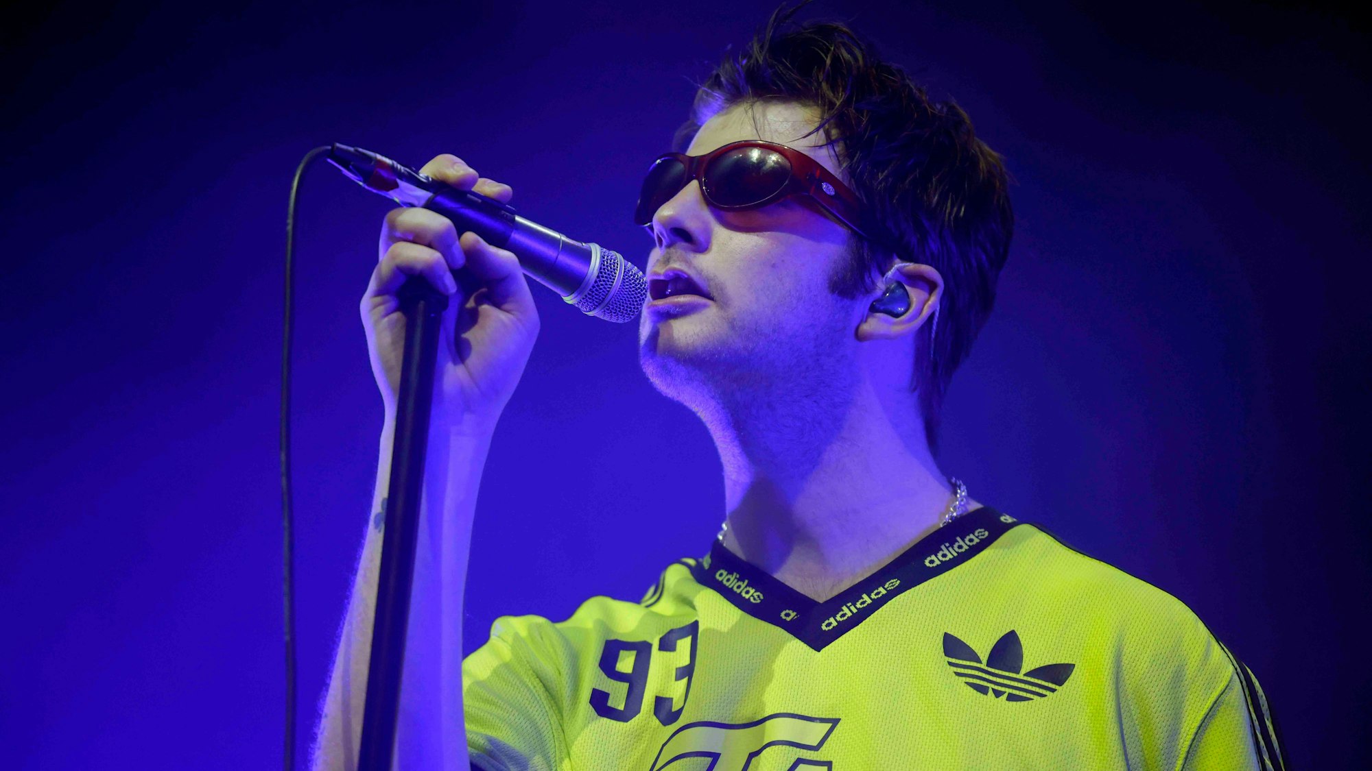 Ein Mann mit Sonnenbrille singt in ein Mikrofon.