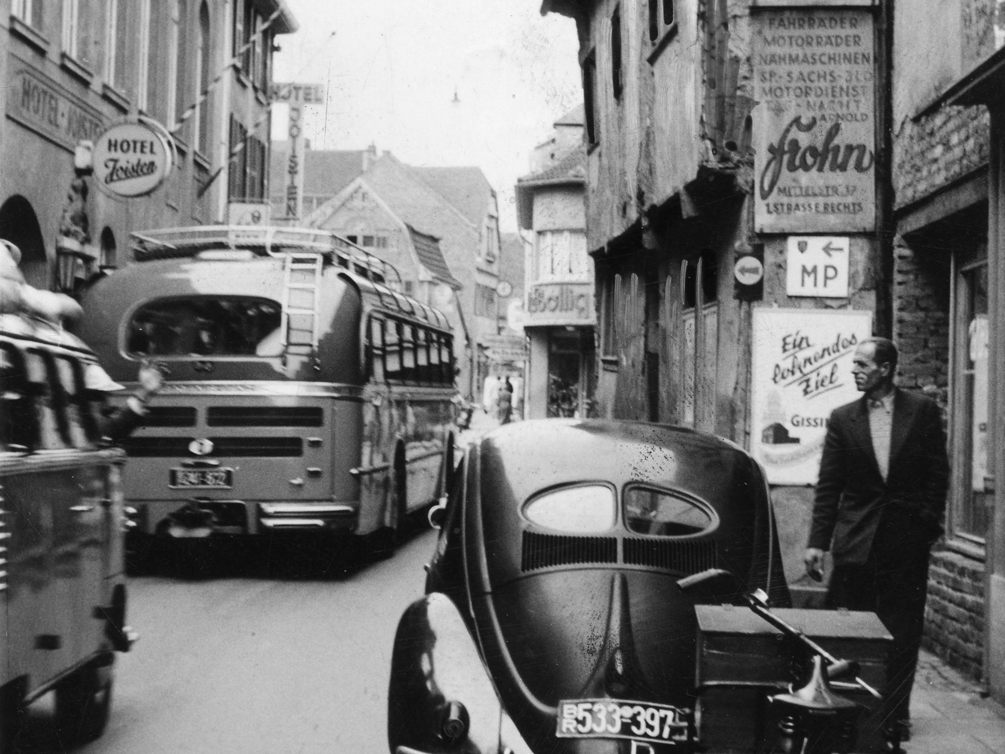 Das historische Bild zeigt die Neustraße zu der Zeit, als sie noch befahren wurde, hier unter anderem von einem Reisebus. Im Vordergrund steht ein VW Käfer am Fahrbahnrand.
