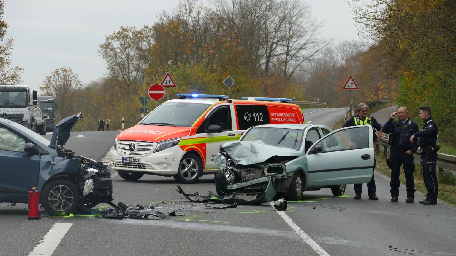 Zwei kaputte Autos stehen auf der Straße, dahinter ein Notarztfahrzeug.