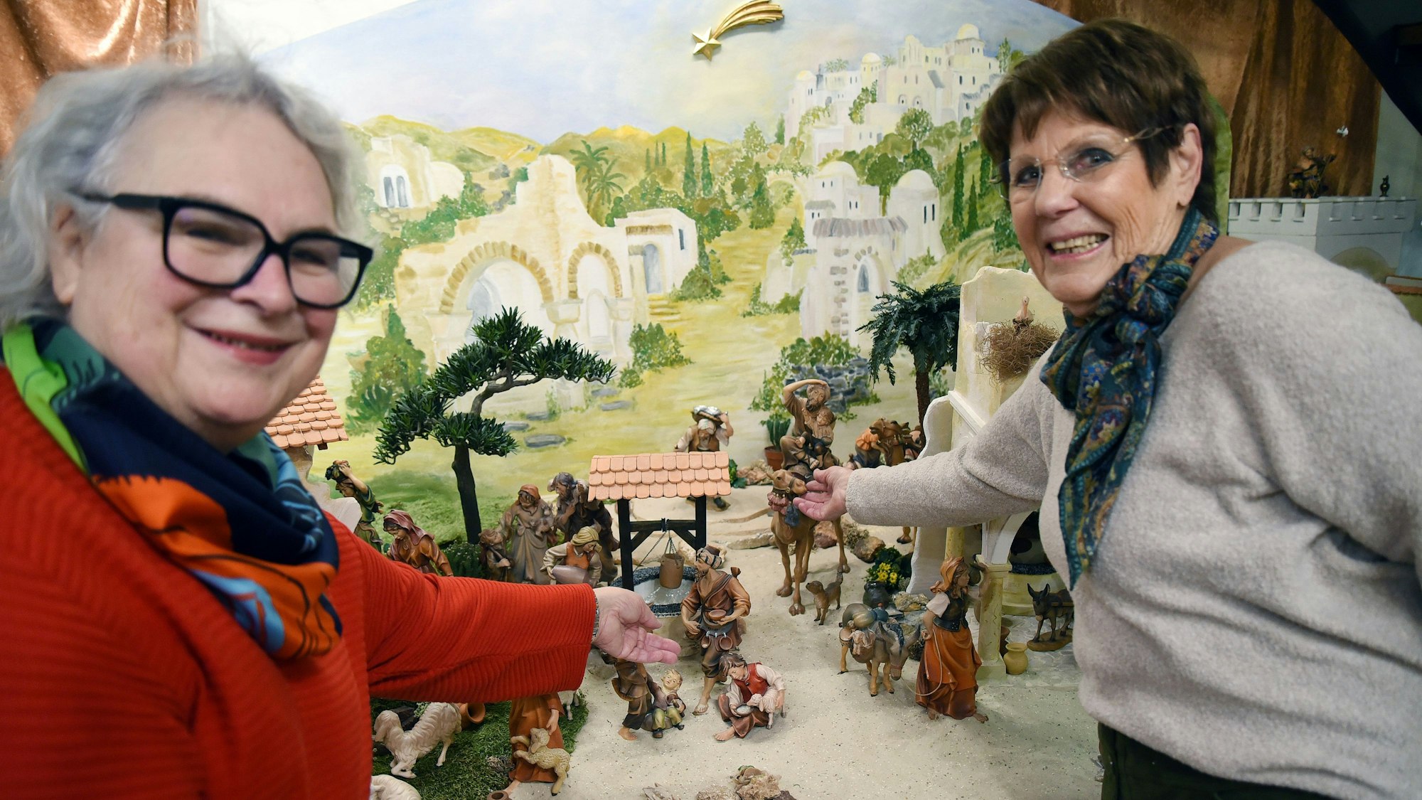 Zwei Frauen zeigen auf ein Ensemble von Figuren in einer großen Krippenlandschaft.