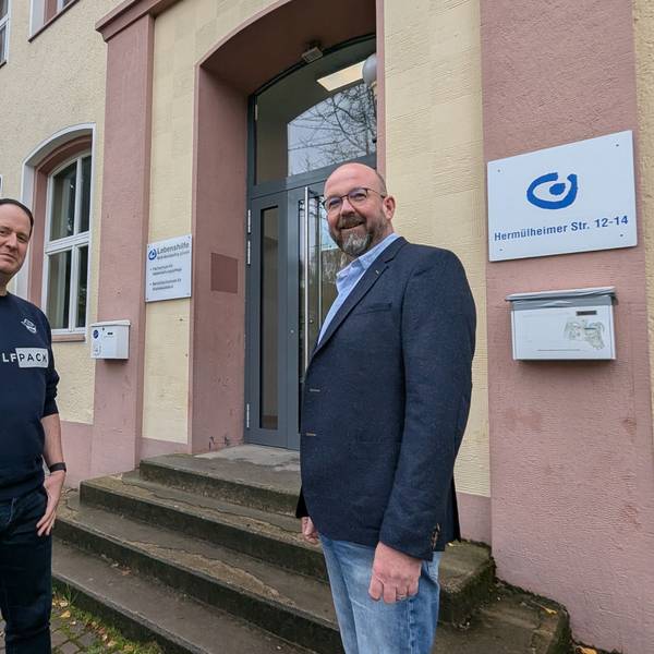 Das Foto zeigt zwei Männer vor dem Eingang zum Berufskolleg im Gebäude der ehemaligen Volksschule.