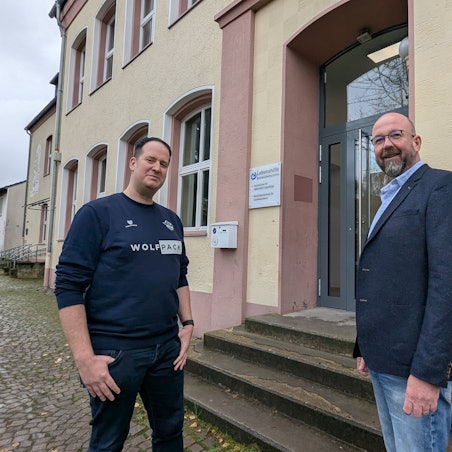 Das Foto zeigt zwei Männer vor dem Eingang zum Berufskolleg im Gebäude der ehemaligen Volksschule.