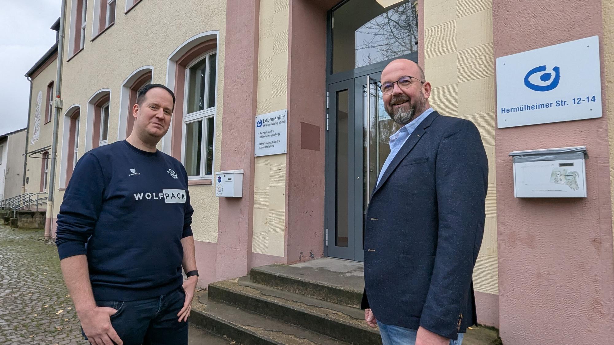 Das Foto zeigt zwei Männer vor dem Eingang zum Berufskolleg im Gebäude der ehemaligen Volksschule.