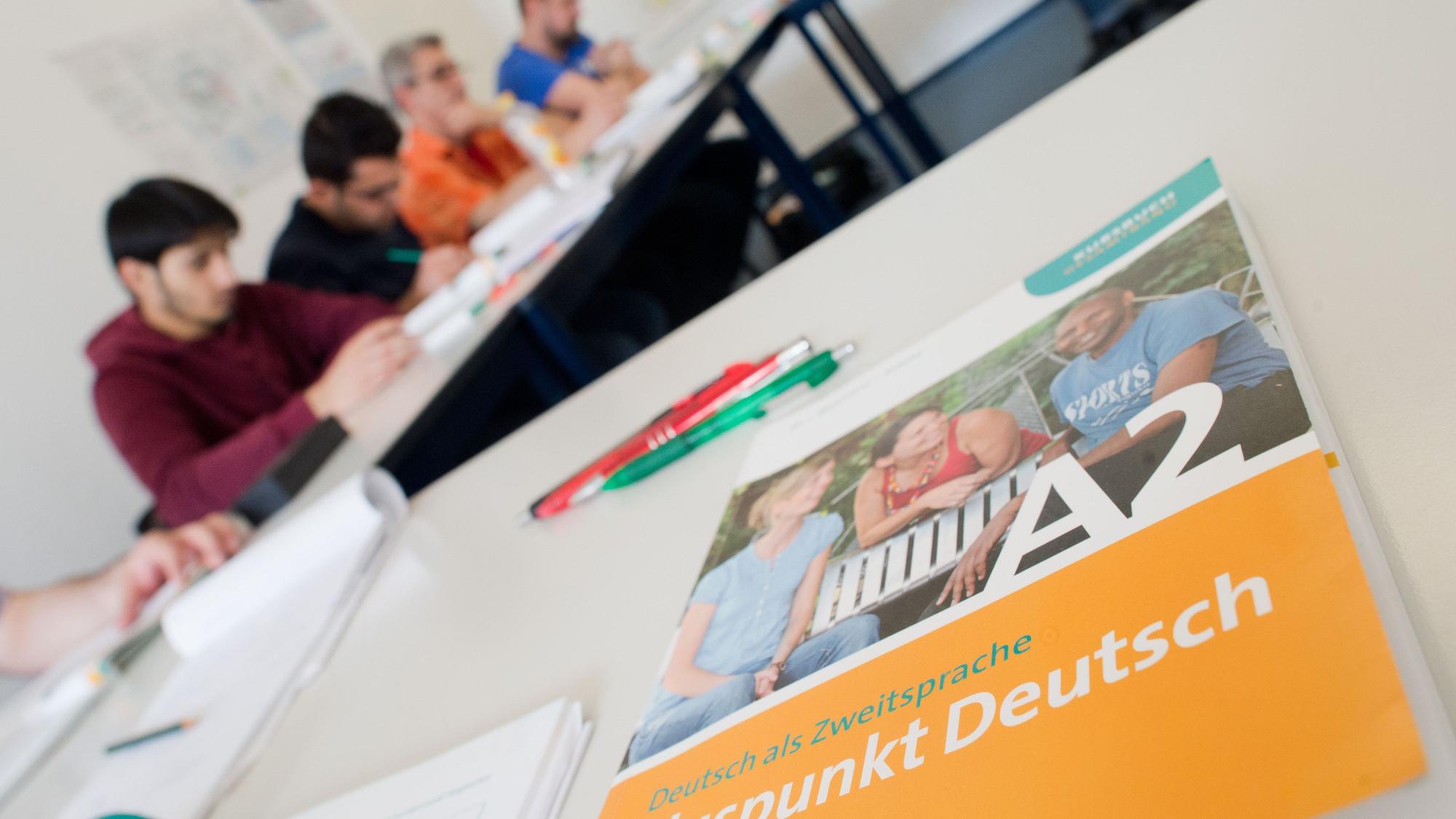 Ein Deutschbuch liegt in einem Integrationskurs. Im Hintergrund sind Kursteilnehmer zu sehen.