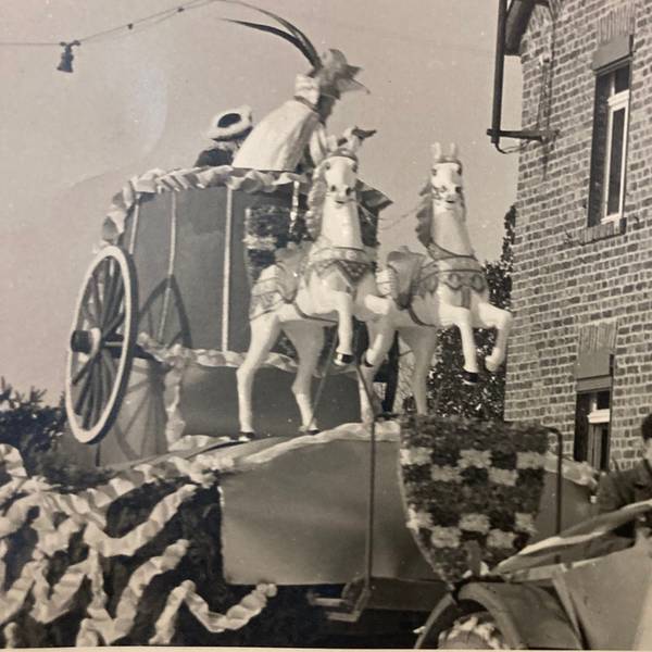Eine Schwarz-Weiß-Aufnahme zeigt einen Karnevalswagen der KG Vernich mit Pferdefiguren, der an einem Backsteinhaus vorbeifährt.