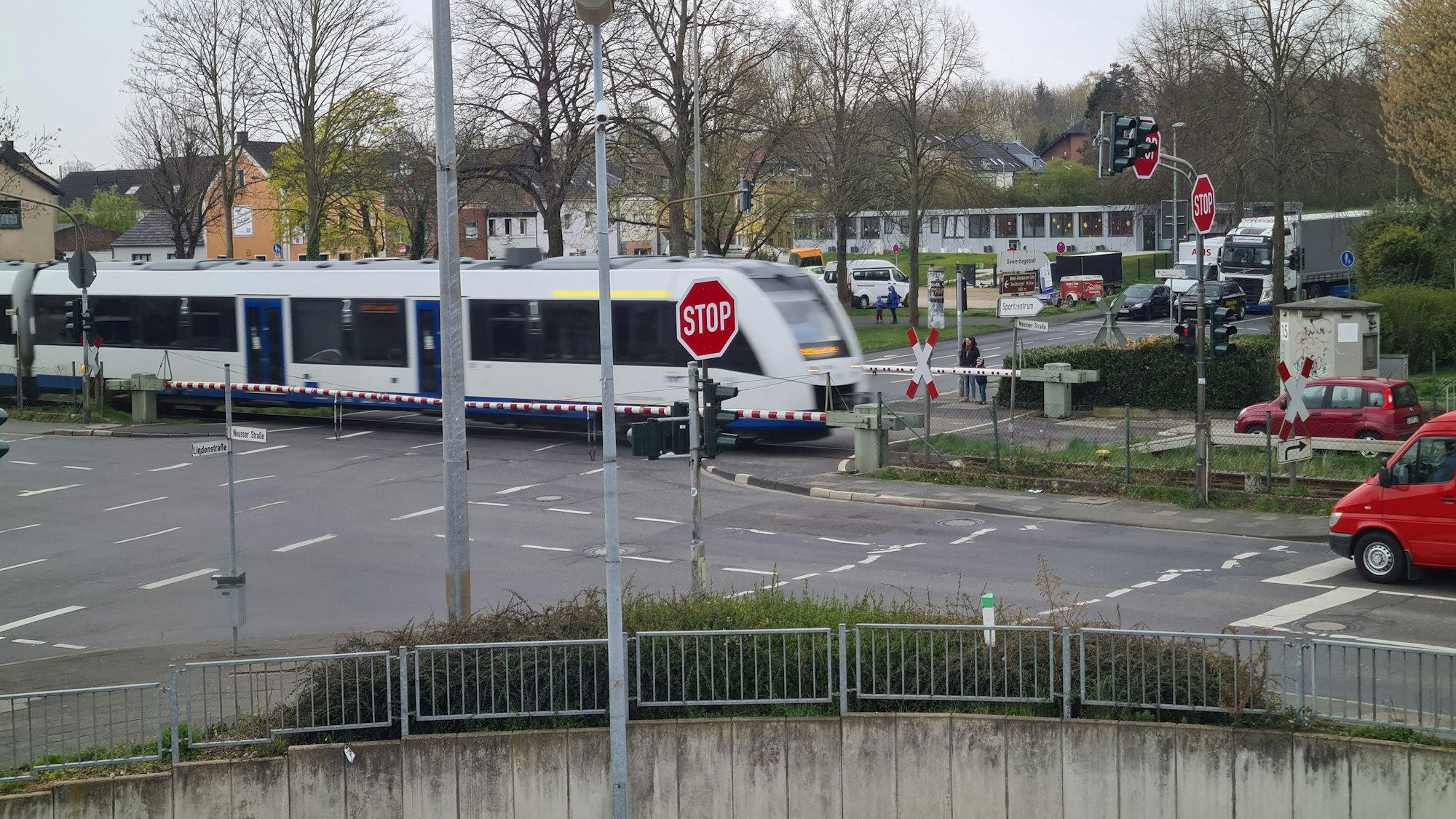 Zu sehen ist ein Zug, der bei geschlossener Schranke über einen Bahnübergang an einer Kreuzung fährt.