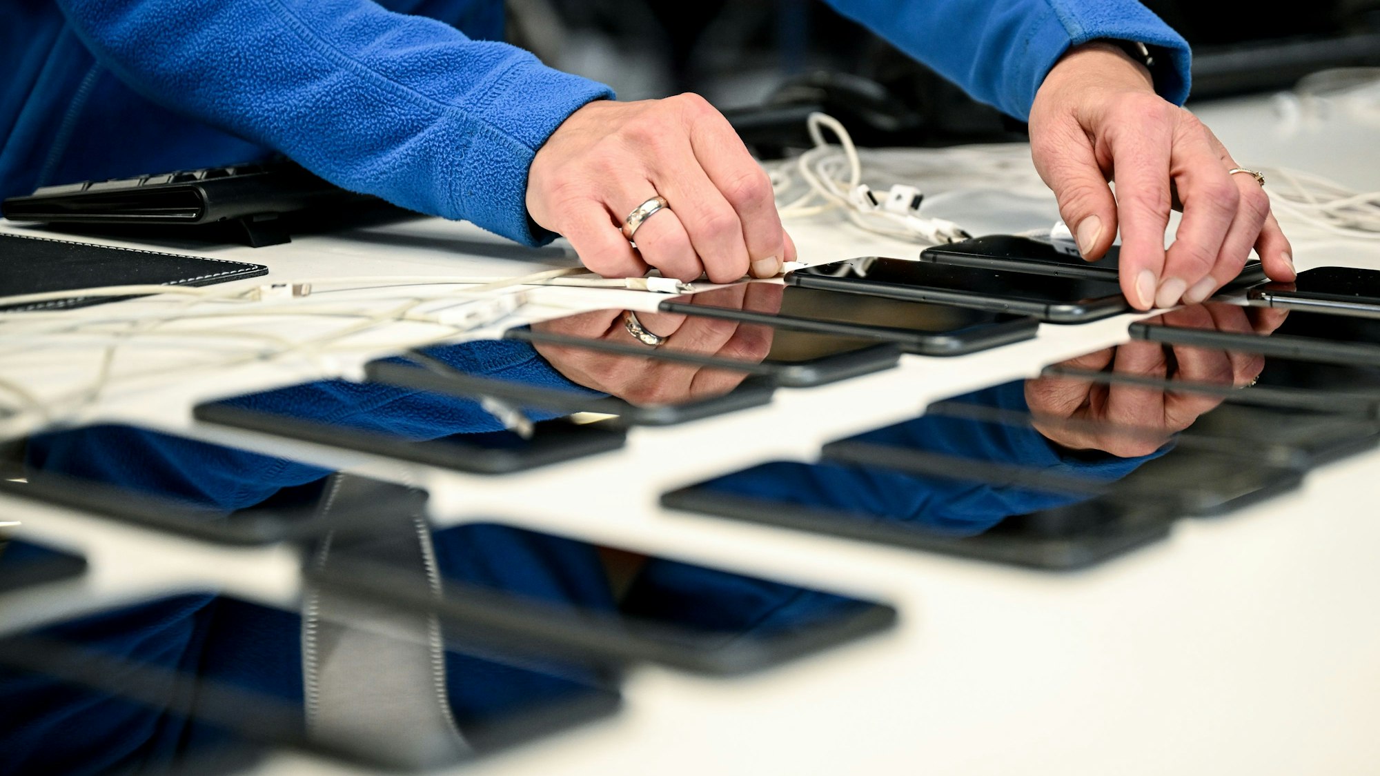 Smartphones liegen auf einem Tisch. Eine Person steckt ein Ladegerät in eines der Handys.