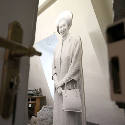 Blick an einer halb geöffneten Tür vorbei in einen Raum, in dem eine lebensgroße Figur von Queen Elizabeth steht.