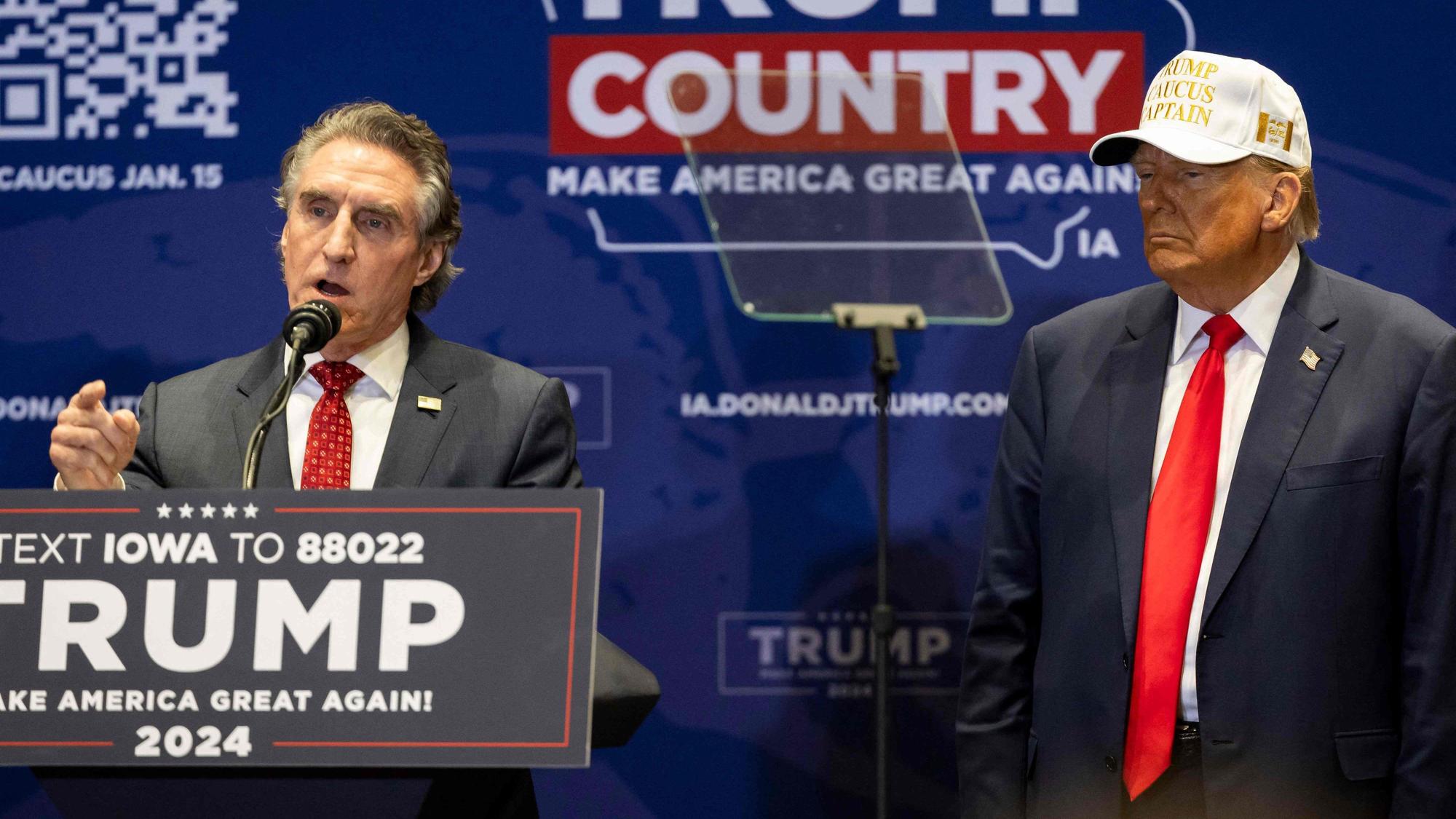 Former US president and Republican presidential hopeful Donald Trump (R) listens as North Dakota Governor Doug Burgum speaks during a "commit to caucus rally" in Indianola, Iowa, on January 14, 2024.